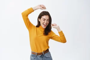 Happy attractive woman dancing and having fun, raising hands up carefree, enjoying music, standing against white background.