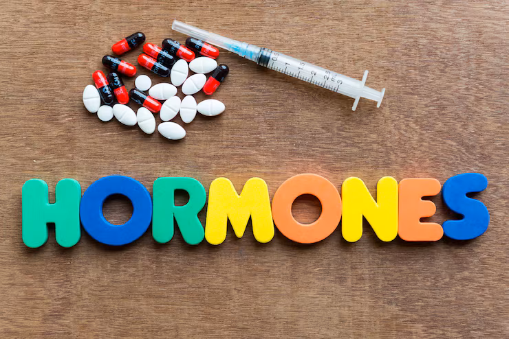 A top-down view shows the word HORMONES spelled out in colorful, capital letters on a wooden surface.