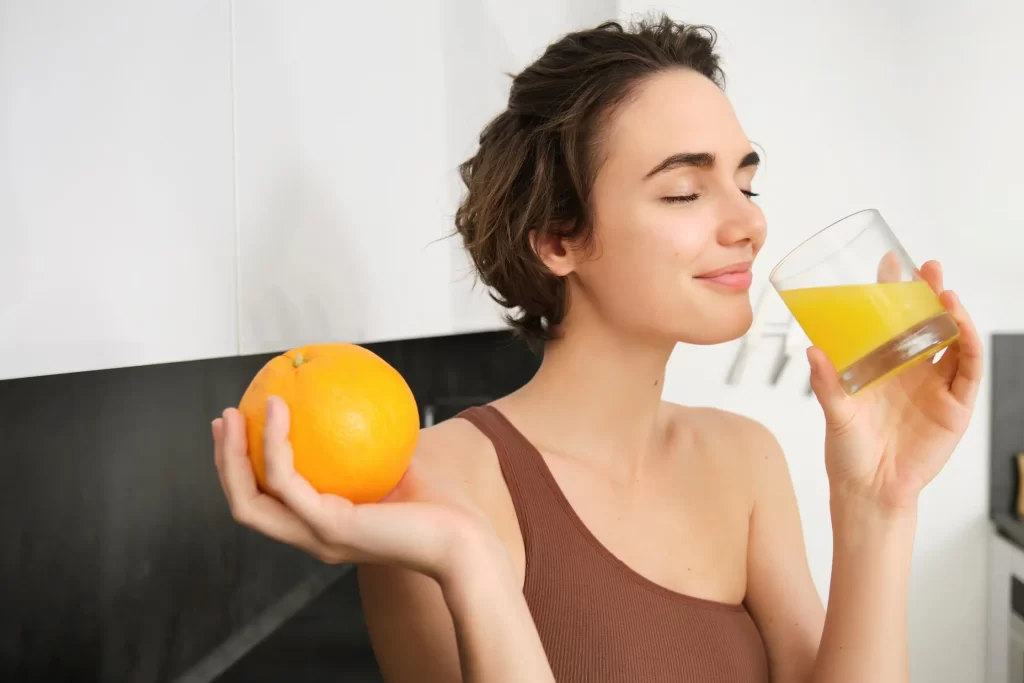 Young woman enjoying a glass of fresh orange juice while holding an orange