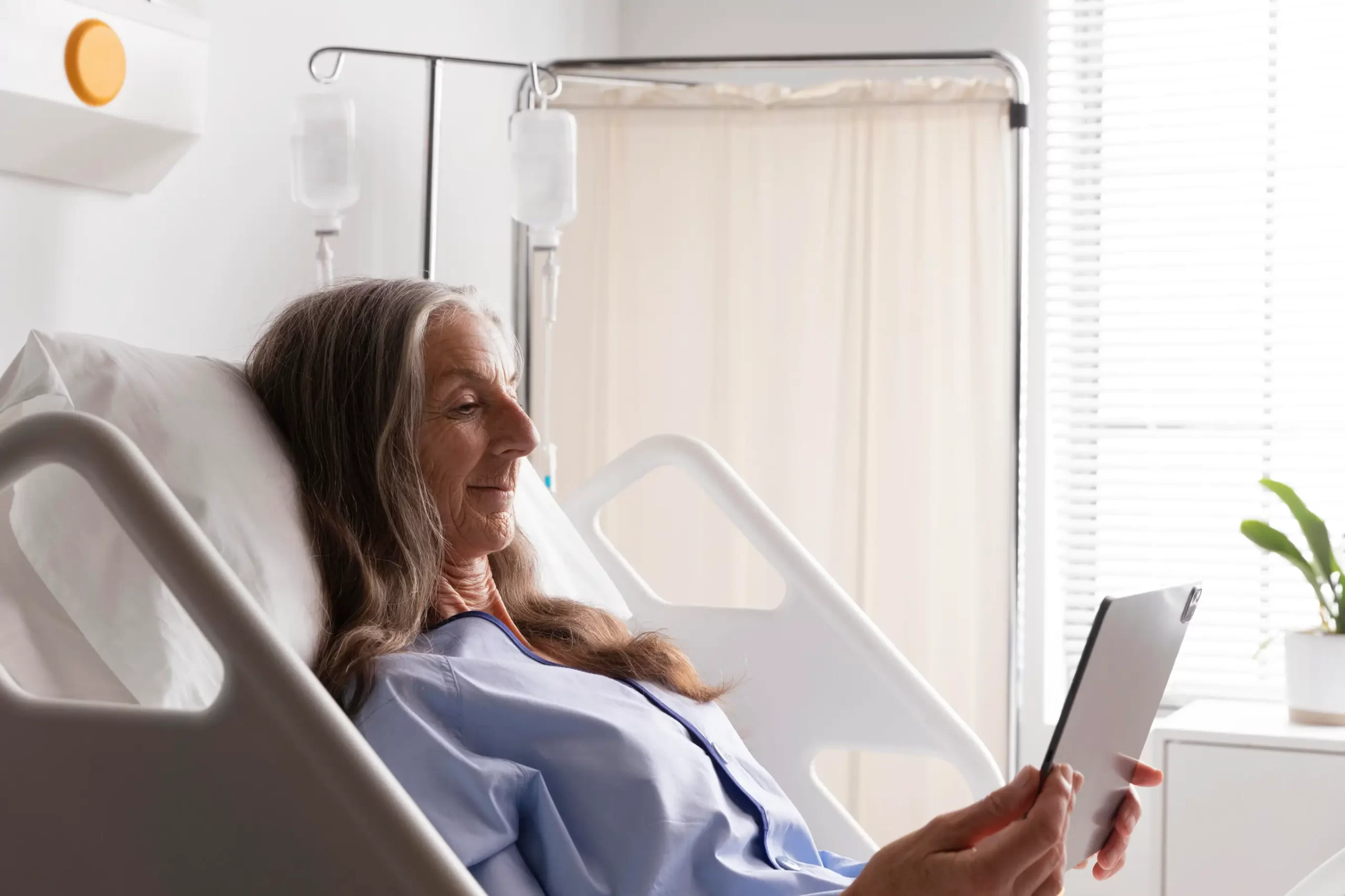 Elderly woman resting in a hospital bed using a digital tablet