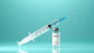Medical syringe filled with clear blue fluid resting against a small glass vial labeled “NAD+ Injection 500 mg” on a reflective turquoise background