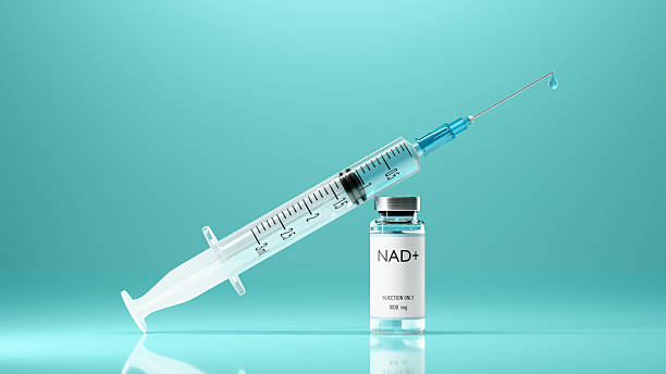 Medical syringe filled with clear blue fluid resting against a small glass vial labeled “NAD+ Injection 500 mg” on a reflective turquoise background