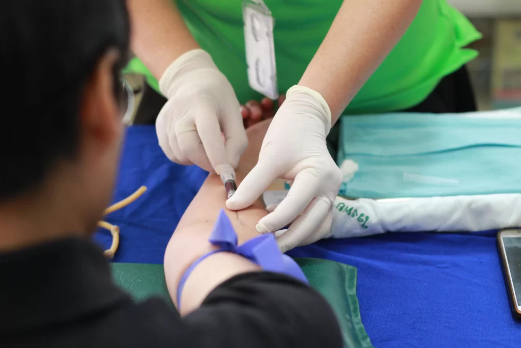 Close-up of a healthcare worker wearing white gloves drawing blood from a patient's arm using a needle and tube
