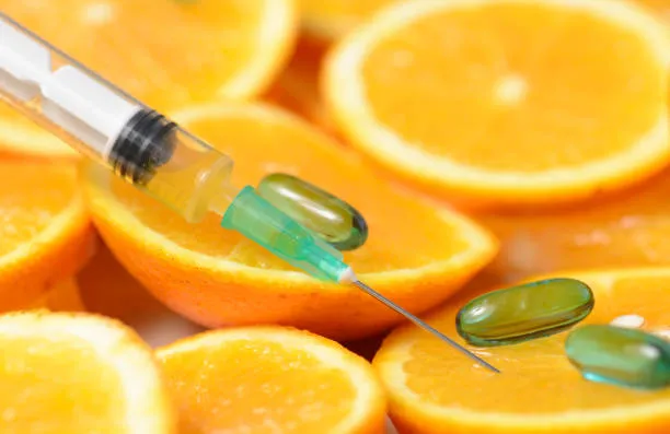 Syringe and vitamin capsules on top of sliced oranges