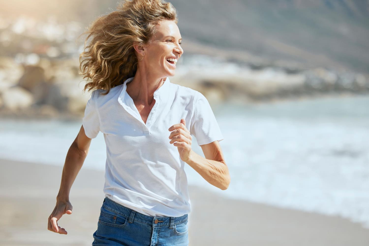 Cheerful mature woman running beach sunny day