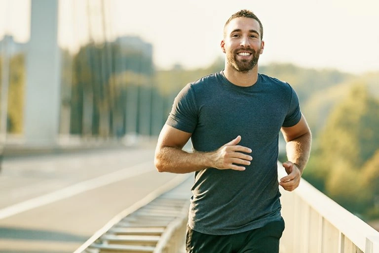 Smiling man in a dark gray t-shirt jogging outdoors on a sunny day