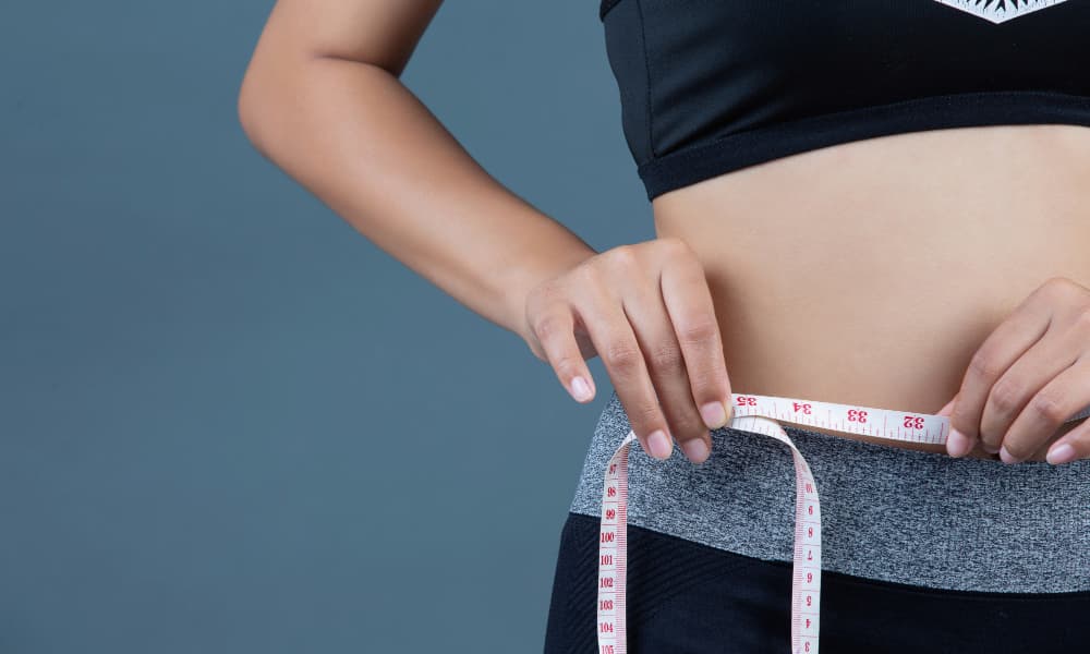 A woman using measuring tape to check waistline progress