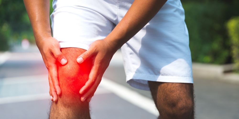 a person outdoors clutching their knee in pain