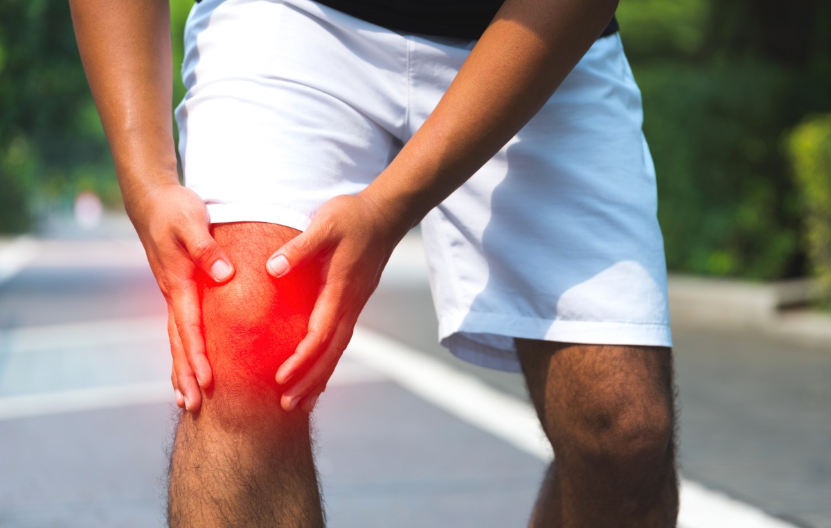 a person outdoors clutching their knee in pain