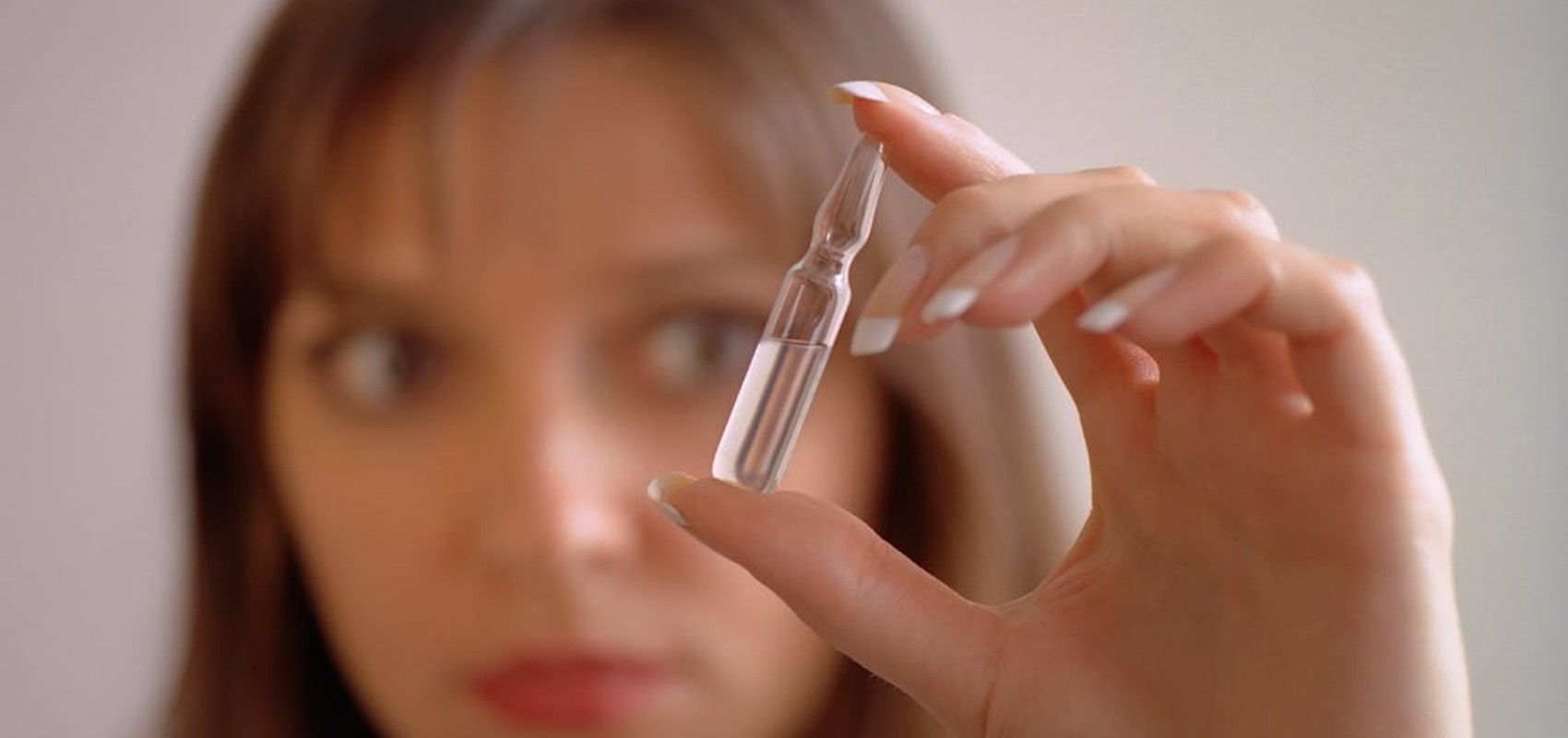 A close-up of a person's hand holding a small, clear glass liquid ampoule