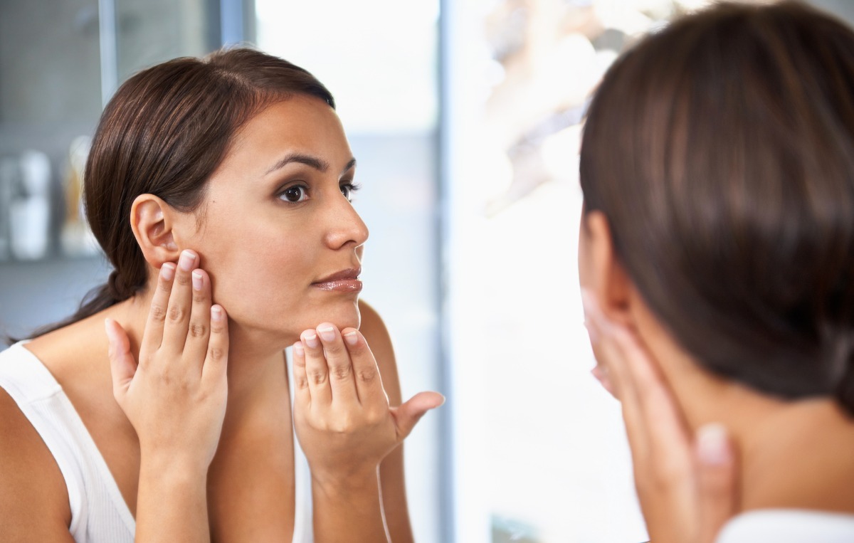 A woman looks closely at her face in a mirror