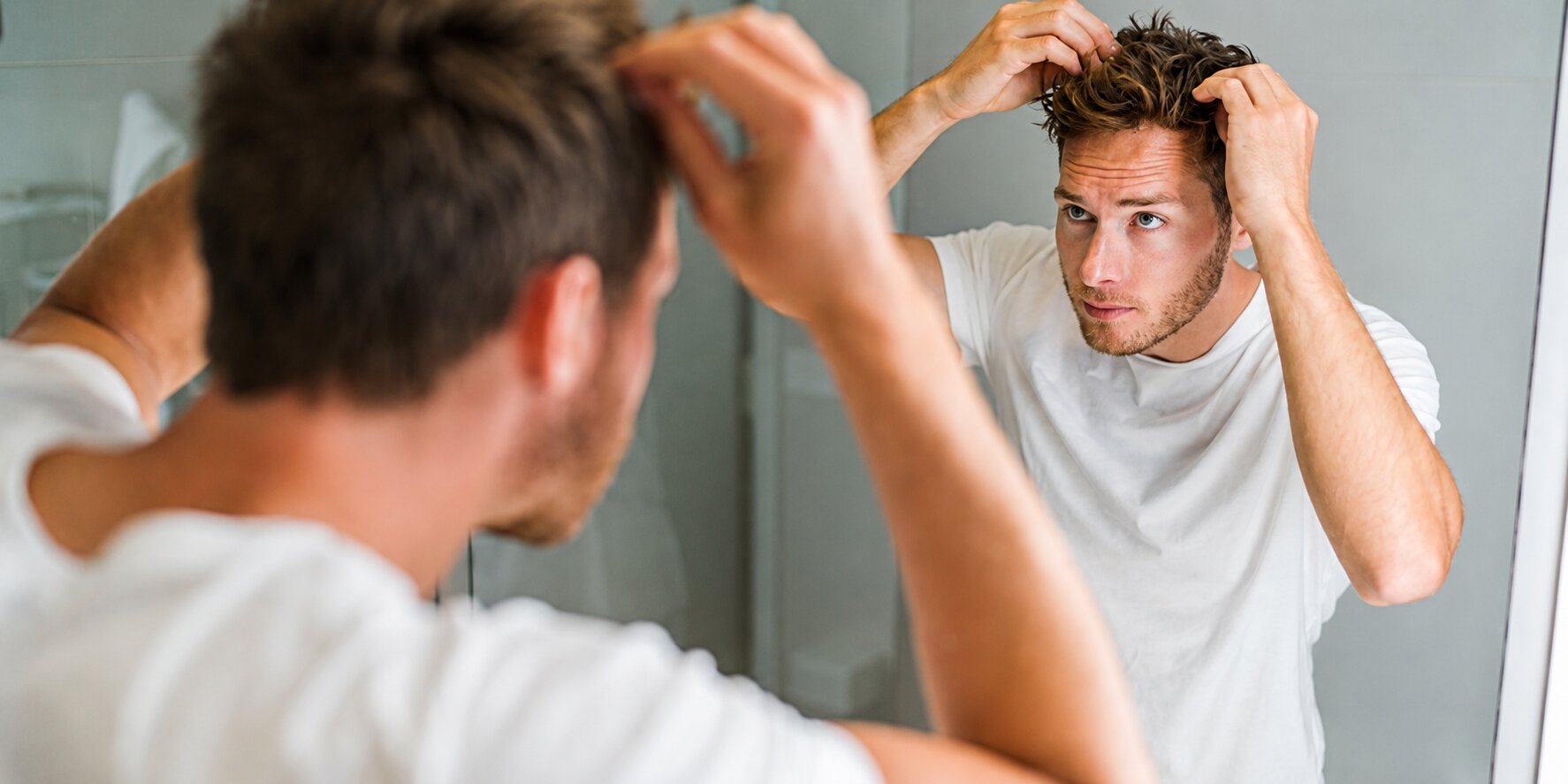 A young man looking at his reflection in a bathroom mirror