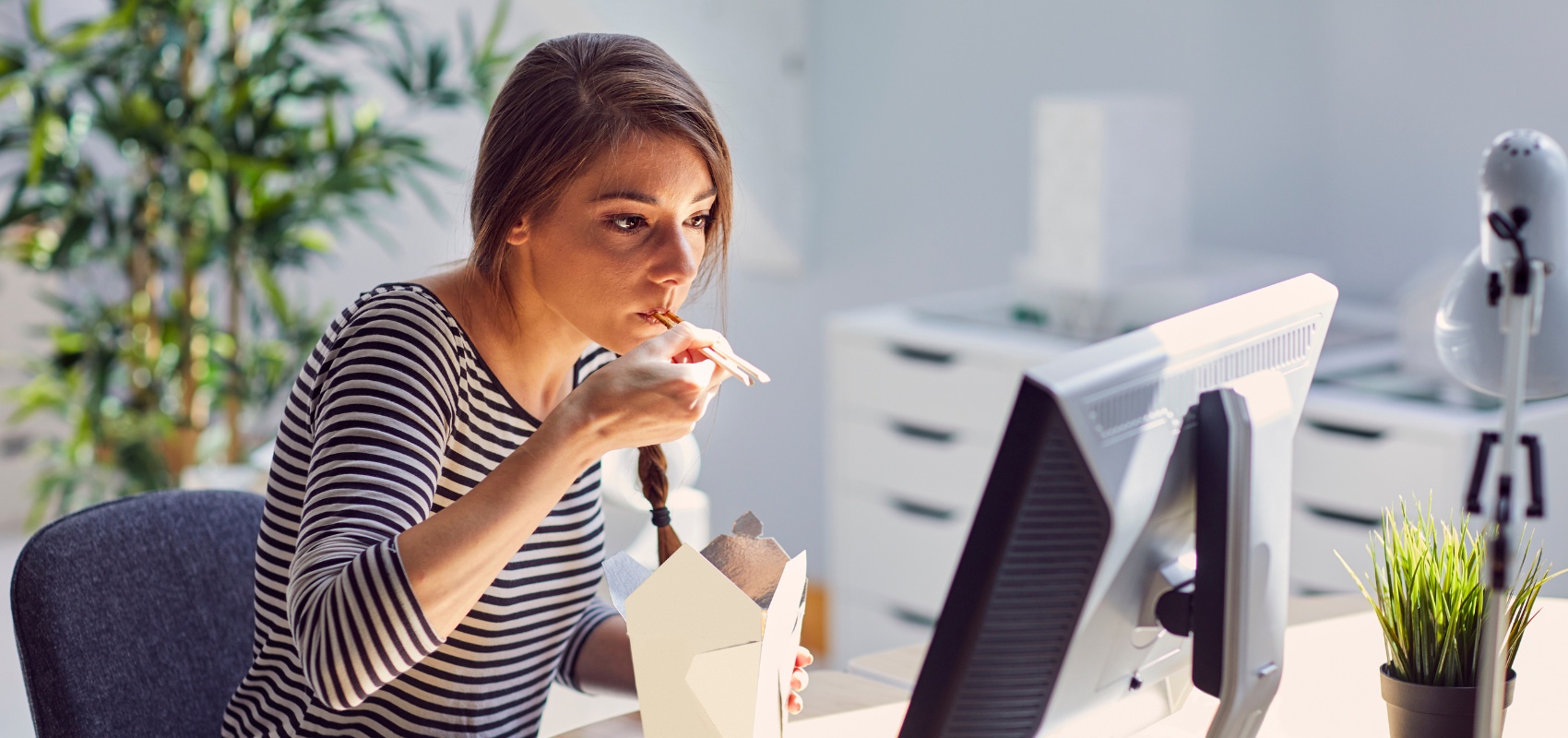 A woman eating takeout food while looking at her computer