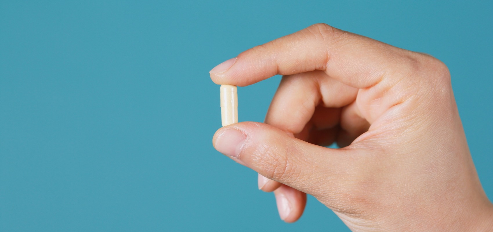 A hand holding a single light yellow capsule