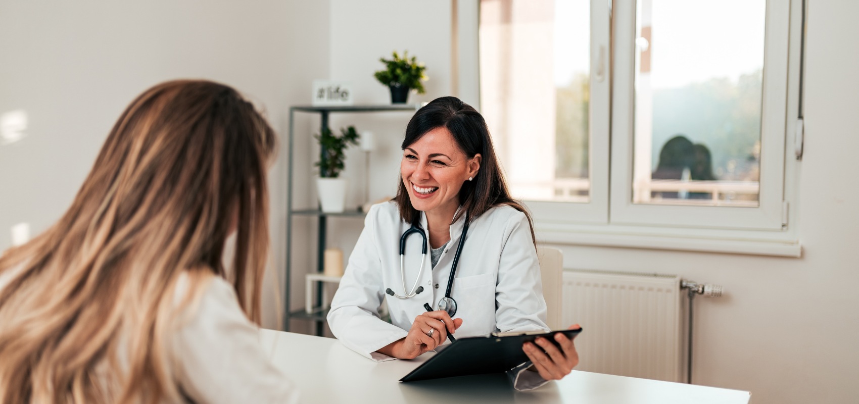 smiling female doctor holding a clipboard talks to a patient