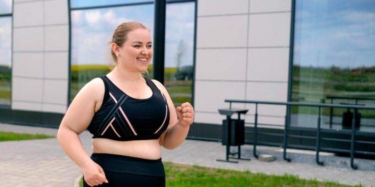 A smiling young woman wearing a black sports bra and matching leggings