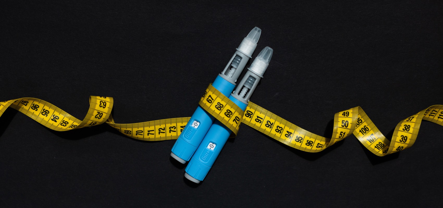 Two blue injection pens wrapped in a yellow measuring tape