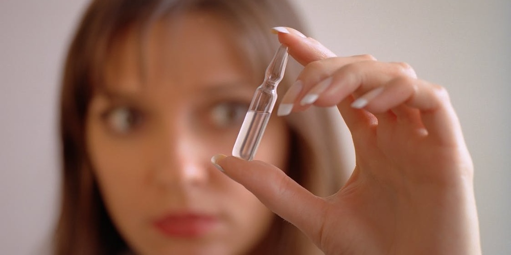 A close-up of a person's hand holding a small, clear glass liquid ampoule