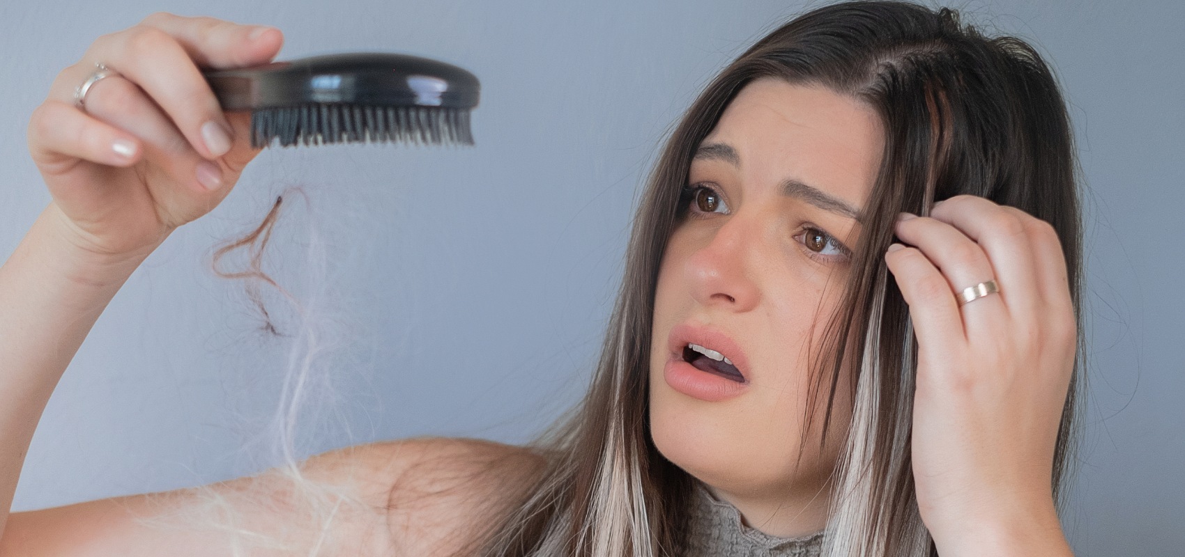 a woman looks at a clump of hair falling from her hairbrush