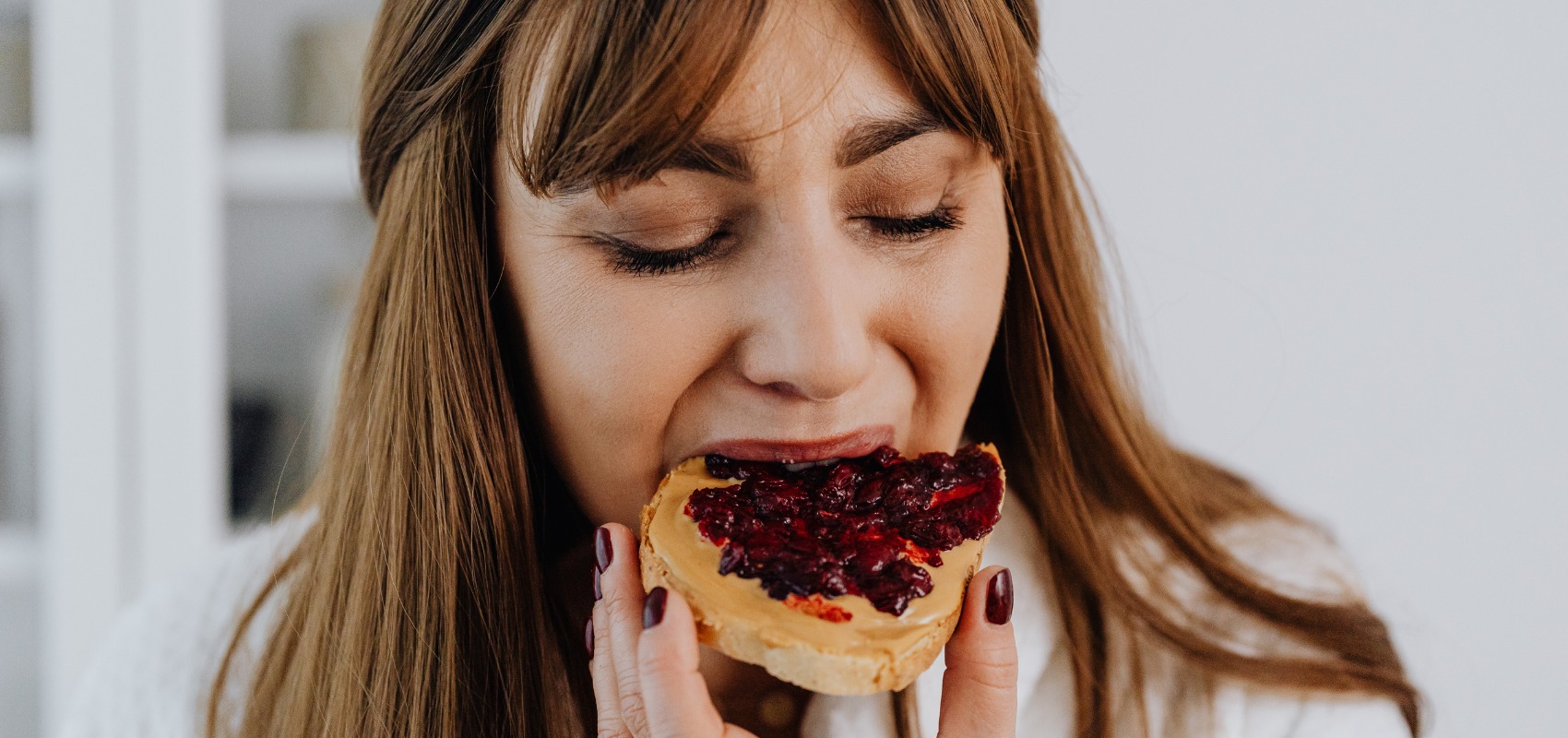 a woman takes a bite of toast topped with peanut butter