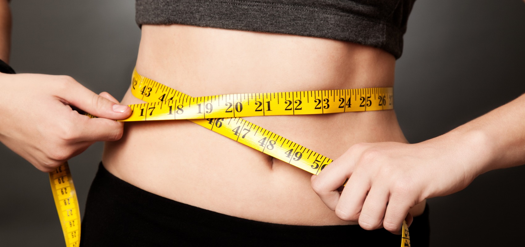 a person wraps a yellow measuring tape tightly around their bare waist
