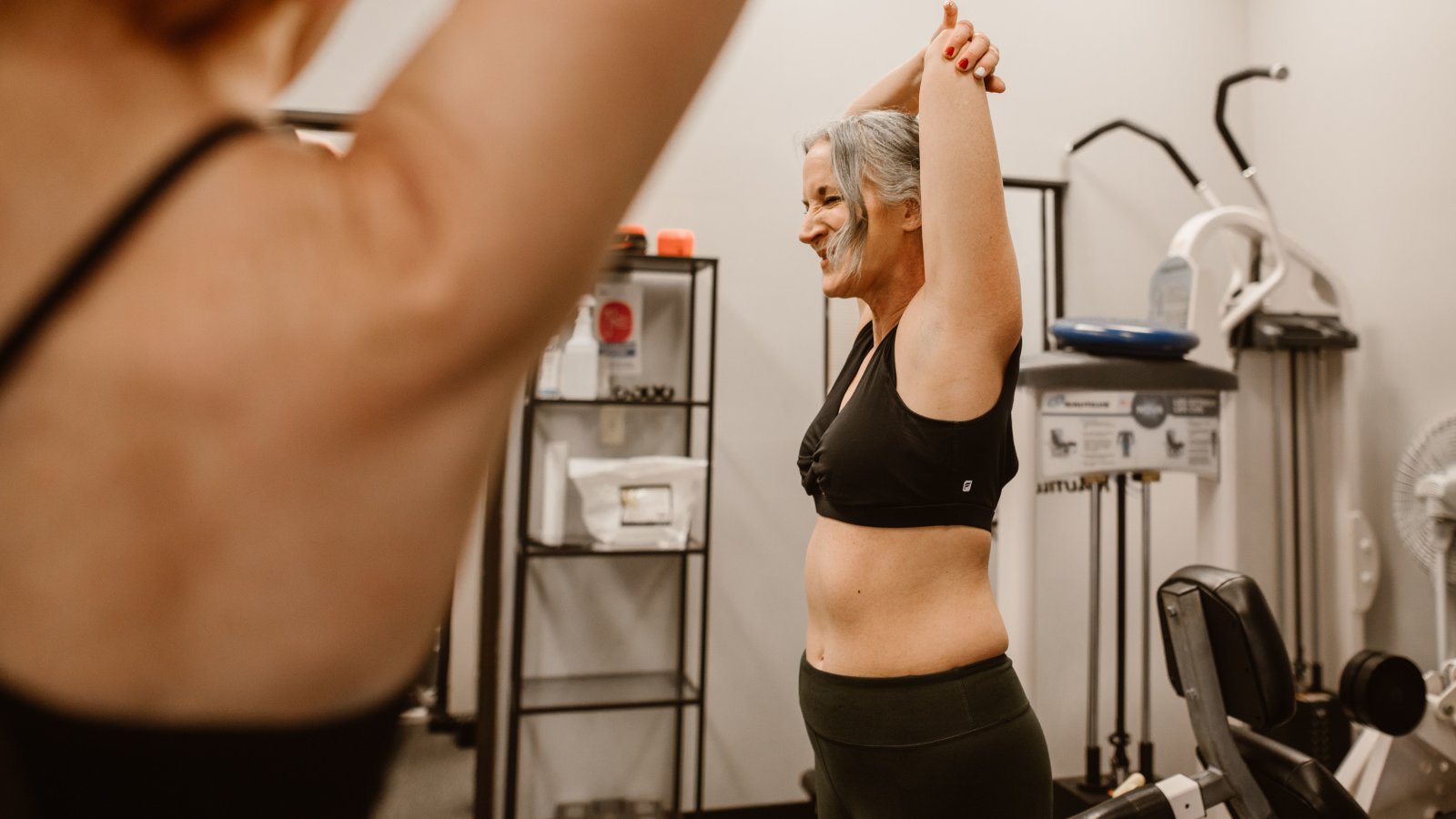 A confident middle-aged woman stretching in a gym, symbolizing wellness and healthy living linked to hormone replacement therapy.