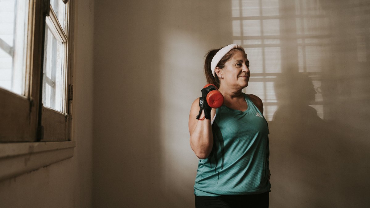 Middle-aged woman lifting a dumbbell indoors, representing fitness and strength important for metabolism.