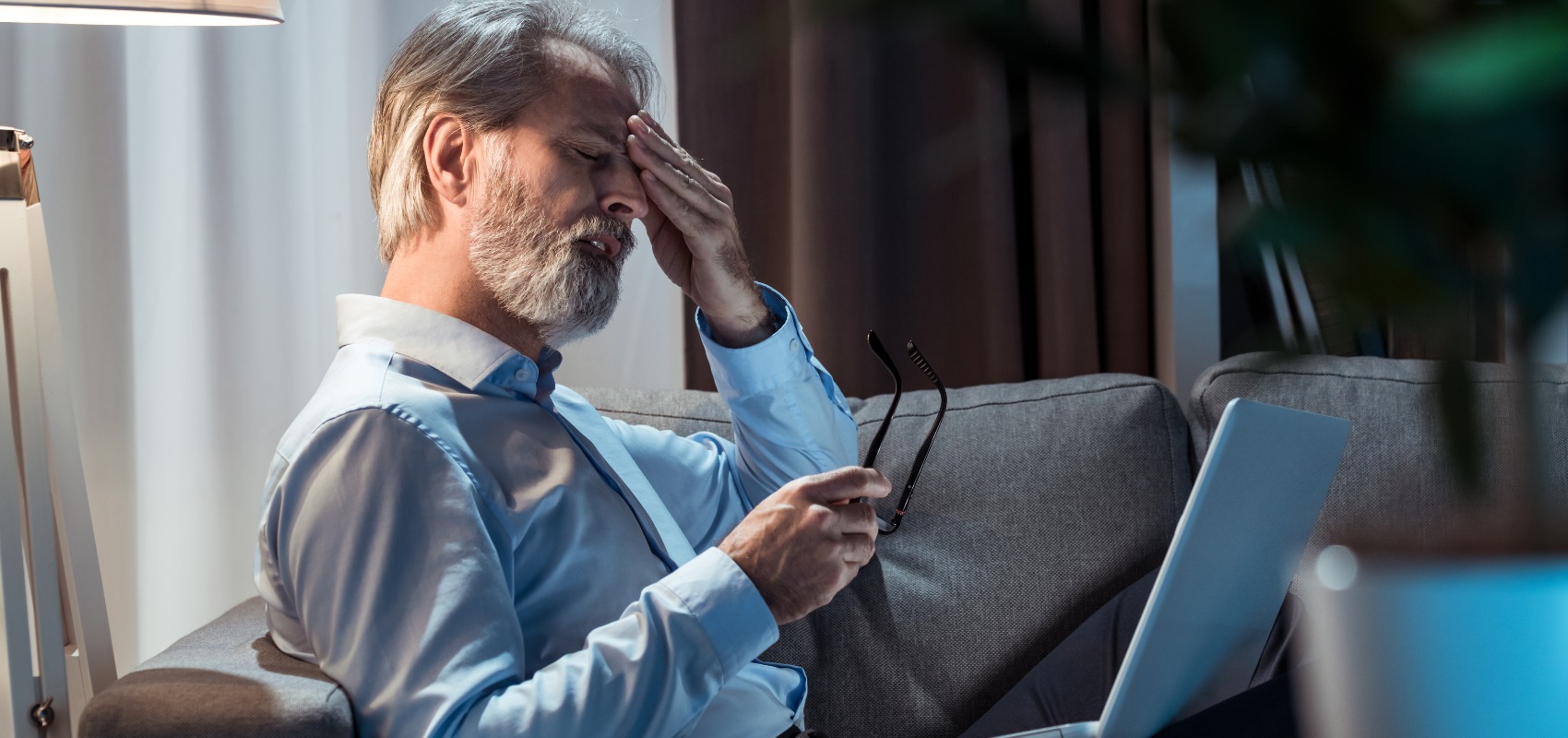 Stressed older man holding his glasses and rubbing his forehead