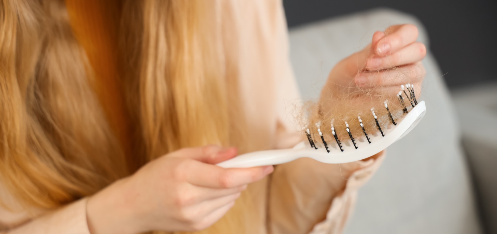 woman holding a white hairbrush filled with loose strands of blonde hair