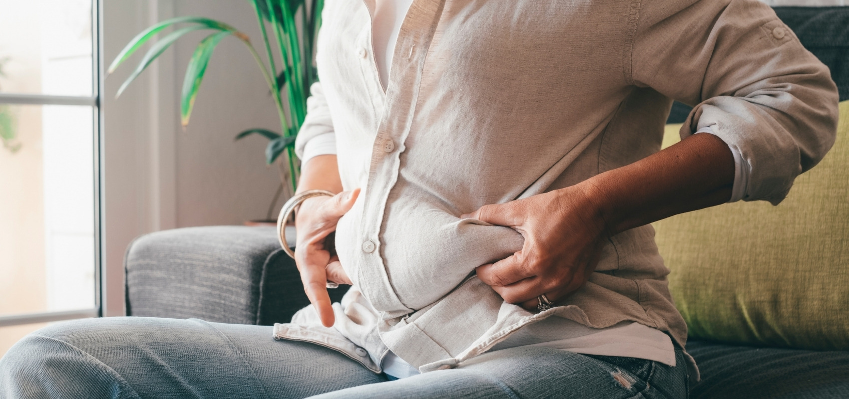 Woman sitting on sofa clutching her bloated stomach