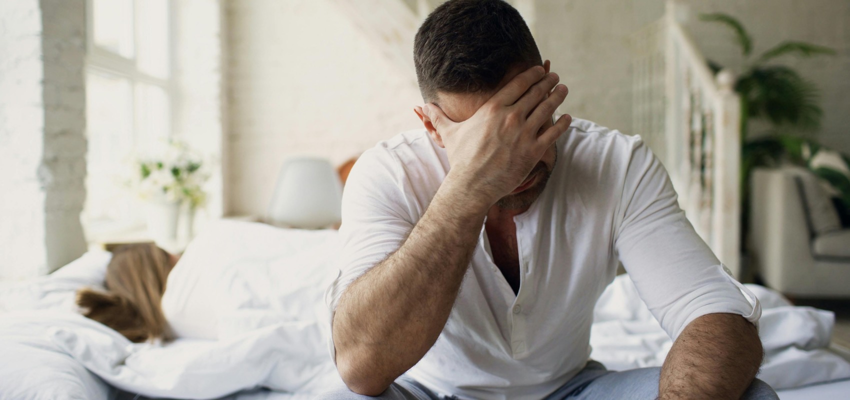 stressed man sitting on bed in bright bedroom