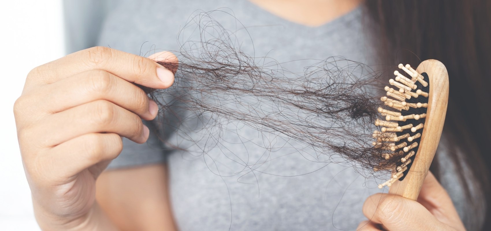 holding a wooden hairbrush with a large clump of loose dark brown hair