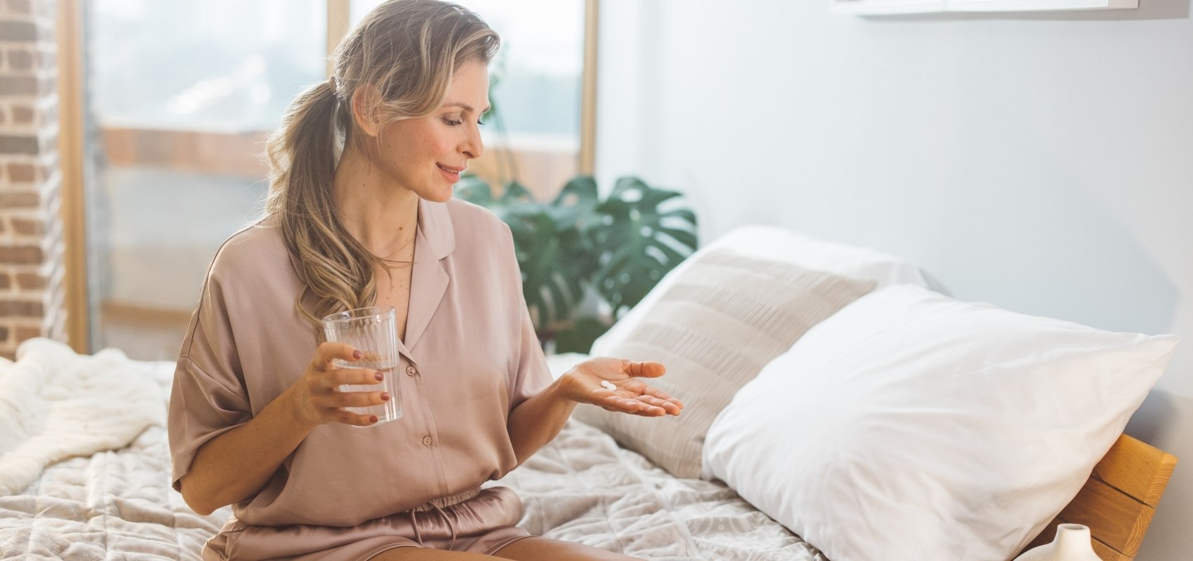 holding a glass of water in one hand and looking down at a pill