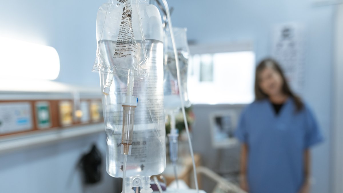 Close-up of an IV drip bag in a hospital with a blurred nurse in the background, illustrating types of IV infusions.